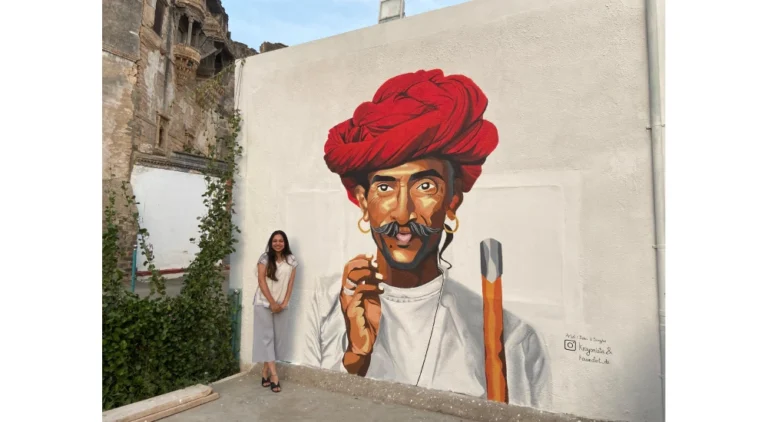 Top wall mural artist in India beside a large public mural of a man in a red turban painted in Bhuj, Gujarat.